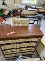 Full view of encyclopedia set arranged in wooden bookshelf with World Atlas volume on top