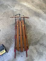 Full overhead view of vintage wooden sled showing wooden slats and metal steering wheel with red metal runners.