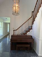 Wurlitzer mahogany spinet piano positioned beside staircase, showing piano and matching bench beneath the keyboard.