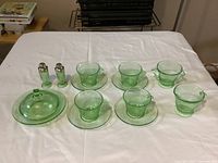Overall view of all 14 pieces laid out on white cloth, showing cups, saucers, shakers, creamer, sugar bowl, butter dish with lid