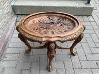 Front view of walnut table showing carved oval top and legs with claw feet, on pavement outdoors.
