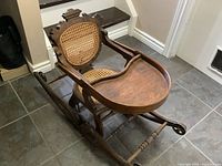 Front angle showing wooden tray, rattan seat and backrest, oak rocking base with wheels