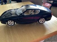 Side profile of the diecast Ferrari 466 GT showing dark blue metallic paint, silver wheels, beige interior through window, and front windshield wiper visible raised.