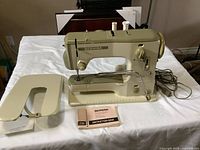 Wide shot of Bernina sewing machine, cover stand, and instruction manual on table.