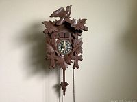 Front view of wooden cuckoo clock showing carved bird and leaves, clock face, chains, and weights.