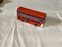 Red Dinky double-decker bus diecast model with side advertisement visible, placed on white cloth background.