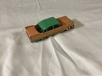Top and side views of Dinky Toys die-cast Plymouth Plaza model car. Shows two-tone green and orange paint with some scuff marks and paint wear.