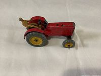 Side angle view of the red Massey Ferguson tractor with yellow wheels and attached metal driver figure in tan paint.