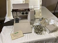 Full view of Elna Lotus S.P. sewing machine, fabric foot pedal, instruction manual, accessories, and original case foam inserts.