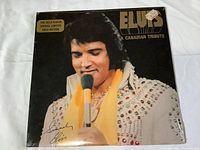 Front cover of Elvis LP record titled A Canadian Tribute, showing portrait of Elvis in white jeweled jumpsuit and yellow scarf, sealed in shrink wrap with special gold edition sticker.