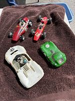 Four vintage toy race cars displayed on a brown towel outdoors, showing overall size and condition.