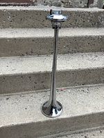 Side angled photo of a long, shiny chrome truck horn with single mount bracket on top, placed on concrete steps.