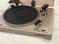 Close view of turntable platter, tonearm and cartridge, dust cover partially raised.