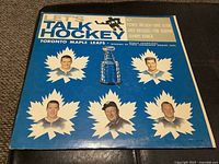 Front cover of the vinyl record sleeve titled "Let's Talk Hockey" featuring six player portraits and a Stanley Cup image, on a blue background.