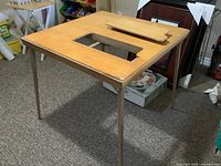 Wooden sewing machine table showing fold-up top with open slot for machine.