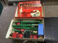 Photo of Meccano metal construction parts in a box with three Meccano instruction booklets on top