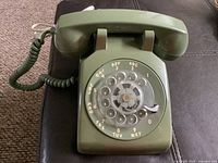 Front view of the rotary dial telephone showing the rotary dial, numbers, and handset in avocado green color.