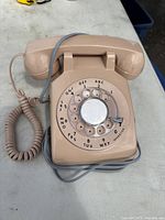 Front view of beige rotary dial telephone showing dial, handset cradle, and coiled cord.
