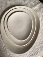 Top view of three nested egg-shaped white porcelain platters on a textured fabric background showing size progression.