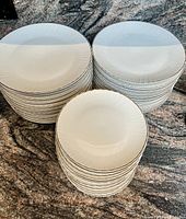 Stack of large dinner plates, small side plates and medium plates showing embossed curved line pattern and gold trim on white porcelain.