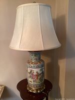 Full view of the lamp showing the porcelain vase base with hand-painted figures and the fabric lampshade on top.