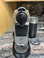 Front view of Nespresso CitiZ espresso machine with attached milk frother on countertop showing chrome and black finish.