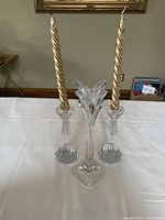 Photo showing two clear crystal candlesticks with gold spiral taper candles and a clear crystal decorative centerpiece with floral cut top on a white surface.