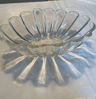 Side angle view of the clear glass decorative bowl showing scalloped petal edges and reflection light effects on surface.