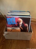 Cardboard box holding over 30 vinyl records with visible cover of Billy Idol album in front.