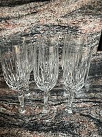 Set of six clear crystal champagne flutes with vertical cut glass design and faceted stems.