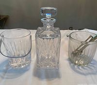 View of whisky decanter centered between two ribbed glass ice buckets, one with handle and one with tongs inside