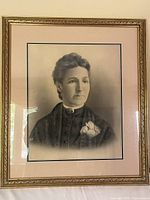 Gold wood frame with ornate detail enclosing a beige matted black and white photographic portrait of a woman.