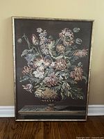 Full view of floral tapestry in wooden frame against wall, showing rich brown background and pink-green floral pattern, sized about 26 x 35 inches.