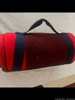 Rolled fleece throw in red and black with navy blue strap and handle, showing side view.