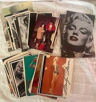 Overview of approximately 40+ glossy postcards laid out showing Marilyn Monroe and other classic Hollywood star portraits primarily in color and black and white