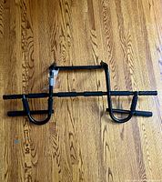 Full view of the black metal pull-up bar laid flat on wooden floor showing the entire structure and multiple foam grip sections.