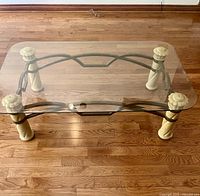 Top view showing clear rectangular glass top and metal frame base with four beige faux stone carved legs.