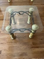 Top-down angled view of square glass top end table showing decorative carved legs and metal frame with arch design.