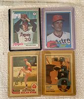Four Nolan Ryan baseball cards in protective sleeves placed on fabric surface. Cards include 1978 Topps Angels card, 1981 Topps Astros card, 1982 O-Pee-Chee Astros card, and 1983 O-Pee-Chee Astros card.