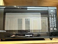 Panasonic black countertop microwave oven front view showing door with mesh window and digital keypad on the right
