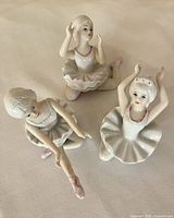 Three porcelain ballerina figurines on cream surface, showing detailed pink accents and poses from above in natural light.