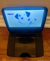 Open RCA portable DVD player powered on showing image of two dogs on the screen, showcasing display condition and device functionality.