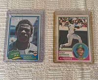 Both Rickey Henderson baseball cards shown in protective plastic cases on white textured cloth background.