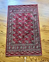 Full view of small silk Persian rug laid on wood floor showing intricate burgundy and cream pattern with borders and repeated motifs.