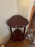 Front and side view of traditional dark brown wooden side table showing clover-shaped top and bottom shelves, and carved legs.
