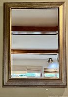 Front view of traditional wall mirror with gilded wood frame reflecting ceiling beams and windows.