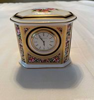 Front view of bone china octagonal mantel clock with floral and fruit pattern, gold trim, and round clock face with Roman numerals.