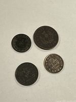 Four antique Canadian coins arranged on a surface, showing various inscriptions and designs including one cent and bank tokens.