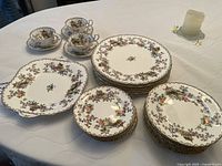 A set of Aynsley china including stacked dinner plates, side plates, and cups with saucers displayed on a table.