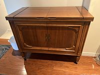 Front view of vintage wooden bar cabinet closed, showing top and double doors with carved details.